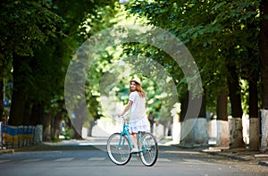 Green urban plantings. Female rides on bike alone at road