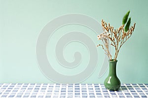 Green vase of dry flower on blue tile table. mint wall background