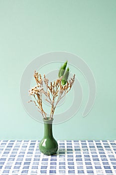 Green vase of dry flower on blue tile table. mint wall background