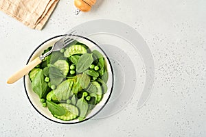 Green vegetable salad with spinach, avocado, green peas and olive oil in bowl on light gray slate, stone or concrete background.