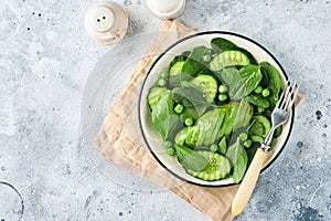 Green vegetable salad with spinach, avocado, green peas and olive oil in bowl on light gray slate, stone or concrete background.