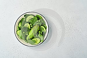 Green vegetable salad with spinach, avocado, green peas and olive oil in bowl on light gray slate, stone or concrete background.