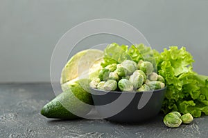 Green vegetables. Bowl with raw brussels sprouts, avocado, cabbage and lettuce on concrete background. Vegetarian food. Selective