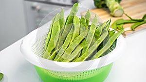 Green vegetables, romano helda beans on the vegetable salad spinner and broccoli on the wooden board. White kitchen table at home