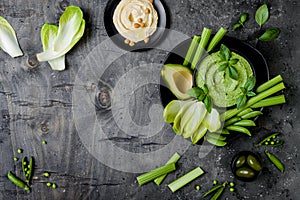 Green vegetables snack board with various dips. Hummus, herb hummus or pesto with fresh vegetables.