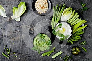 Green vegetables snack board with various dips. Yogurt sauce or labneh, hummus, herb hummus or pesto with fresh vegetables.