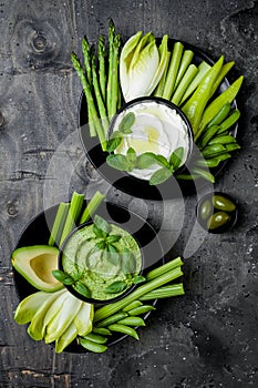 Green vegetables snack board with various dips. Yogurt sauce or labneh, hummus, herb hummus or pesto with fresh vegetables.