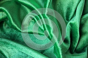 Green velour fabric texture. Wavy folds background. Fragment of a drapery dark green cloth material