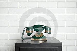 Green vintage corded phone on small black table near brick wall