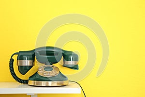 Green vintage corded phone on table against yellow background. Space for text