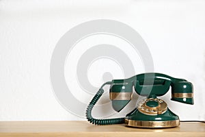 Green vintage corded phone on wooden shelf near wall. Space for text