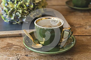 Green vintage cup of coffee on old wooden table, hydrangea flowers