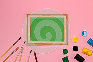 green vintage school blackboard as copy space on pink background, next to it are brushes and paint