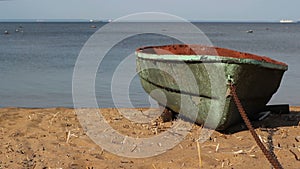 Green virid boat on the chain, on the sandy seashore. The sea is calm. On the horizon stones, gulls, ships