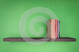 On the green wall is a dark wooden shelf on which there are three books of different colors