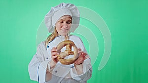 Green wall studio baker woman with a cute large smile playing with a fresh pretzel in front of the camera she moving