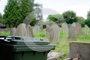 Green waste wheelie bin seen located by the side of an old cemetery.