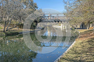 Green water of San Antonio River with a reflection of the trees and bridge at River Walk- Texas