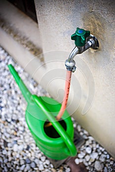 Green watering can on water tap