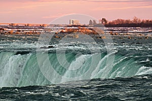 Green waters of Niagara river dashing downd from the edge of Horseshoe Falls in front of spectacular sunset sky