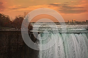 Green waters of Niagara river dashing downd from the edge of Horseshoe Falls in front of spectacular sunset sky