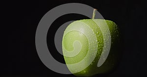 Green wet apple rotates hanging on a dark background, isolated.