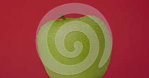 Green wet apple rotates hanging on a red background, isolated.
