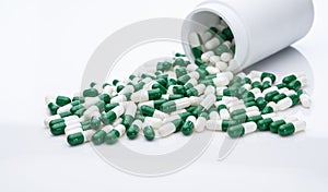 Green and white capsule pills spilled out of a white plastic bottle. Pharmaceutical industry. Prescription drug. Healthcare and