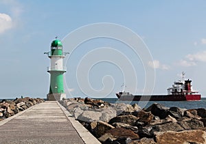 Green and white lighthouse and cargo ship leaving port