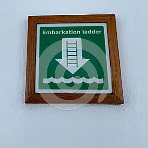 A  green and white sign the tells cruise ship passengers where the embarkation ladder is to get to where the life rafts are