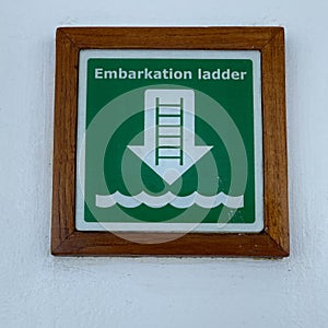 A  green and white sign the tells cruise ship passengers where the embarkation ladder is to get to where the life rafts are