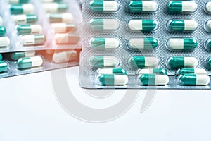 Green-white small capsule pills in blister packs on white table and blurred background of pills pack. Vitamins and supplements.