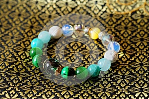 Green and white tone lucky stone bracelet. green moss agate, Green tiger`s eye, jade on Thai traditional golden tone fabric backgr