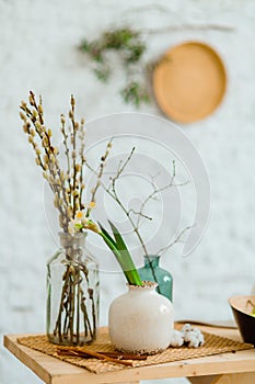 Green willow branches and daffodils in simple vases on the table with Easter decor