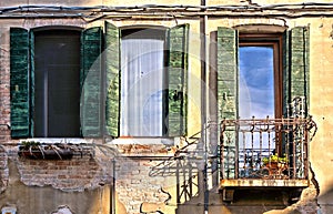 Green windows and balcony with old building facade and brick texture in Venice, Italy