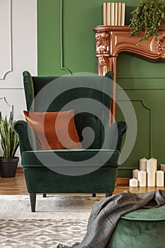 Green wing back chair with orange pillow in luxury living room interior