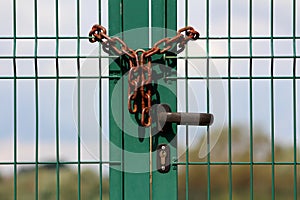 Green wire fence doors with metal frame and black door handle connected with rusted chain and locked with padlock