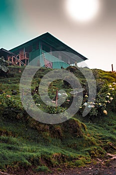 Green wooden country house on top of a beautiful hill adorned with flowers and with a stone shedron in the middle of a cloudy day photo