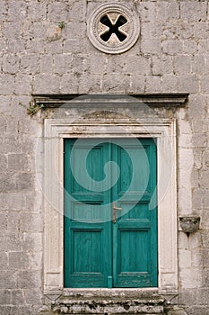 Green wooden door framed by stucco platbands with rosette window on top