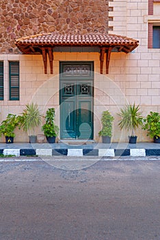 Green wooden door with red tile canopy above and window shutters on stone bricks wall