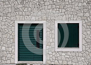 green wooden door with shutters closed on window against stone wall on house