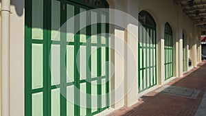 Green wooden folding arches doors on vintage mastic yellow building with empty stone tile pavement