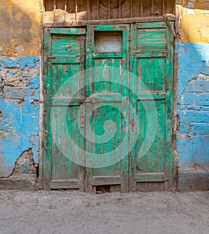 Green wooden grunge weathered abandoned door on dirty wall painted in yellow and blue