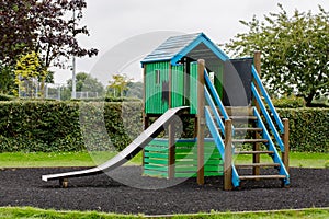 Green wooden house with slider on empty playground