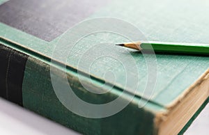 A green wooden pencil is placed on the hardback or textbook. selective focused