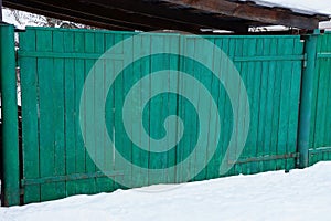 Green wooden rural gate on the street in white snow