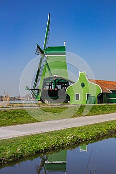 Green wooden windmill reflected in the canal of Zaanse Schans