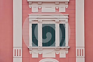 Green wooden window with shutters in white frame on pink wall