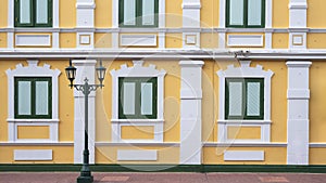 Green wooden windows on vintage yellow and white building wall with street lamp post on empty stone tile pavement