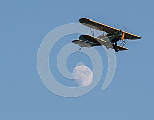 Green antique bi plane with yellow trim flying past full moon